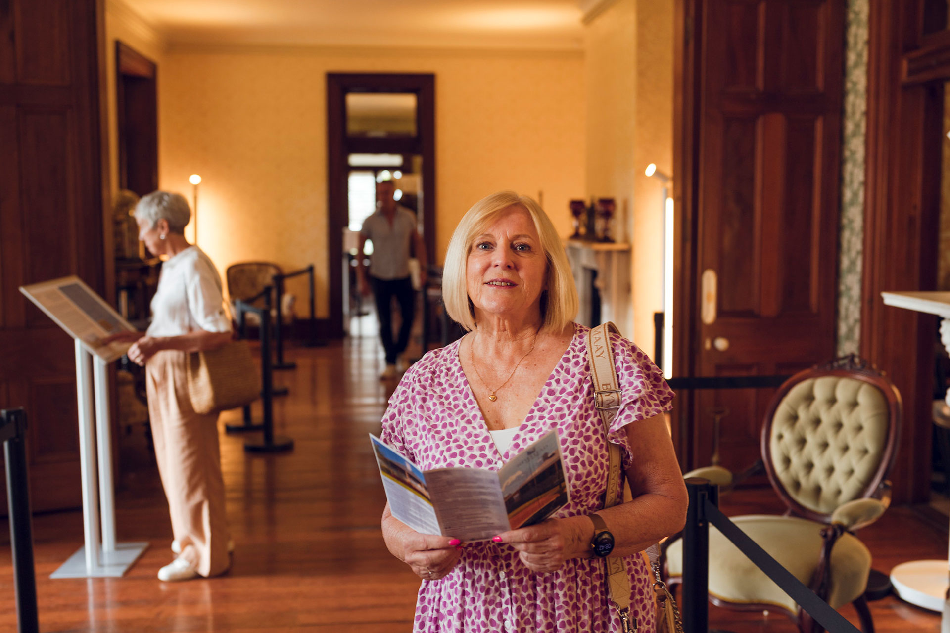 Three people walking through the drawing room with dark wood floors vintage furniture and decorative items at Newstead House