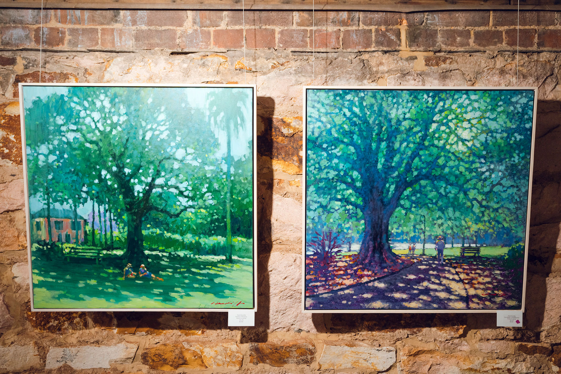 Two paintings of large shady trees hung on a rustic wall