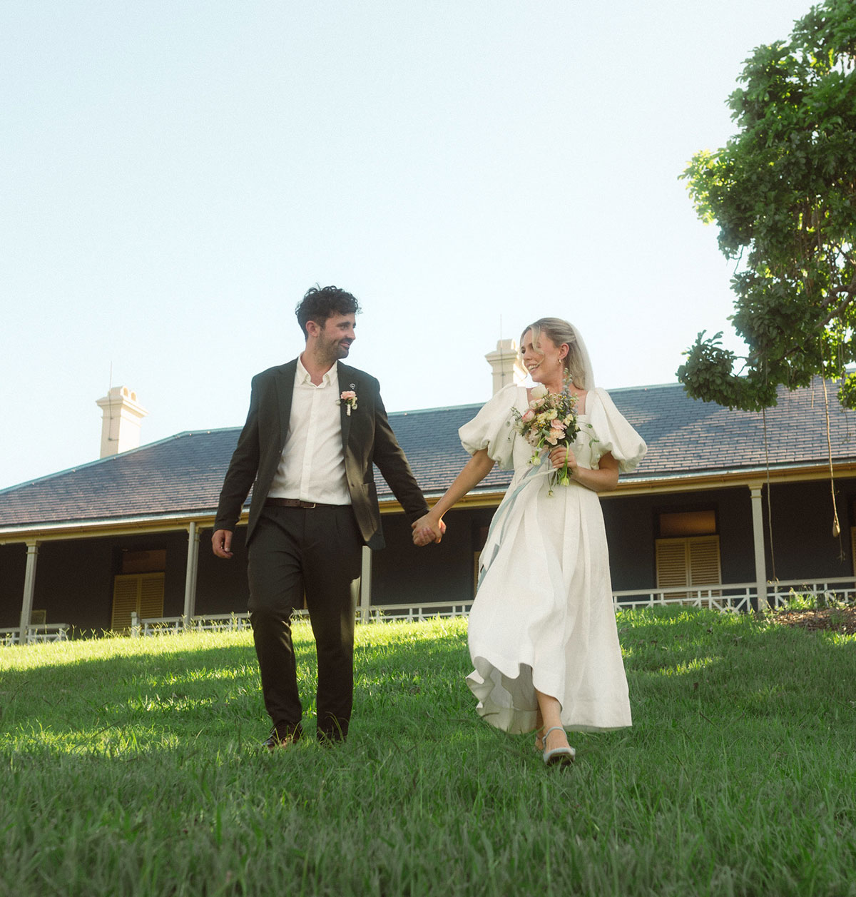 Bride and groom holding hands walking across the grass with Newstead House in the background