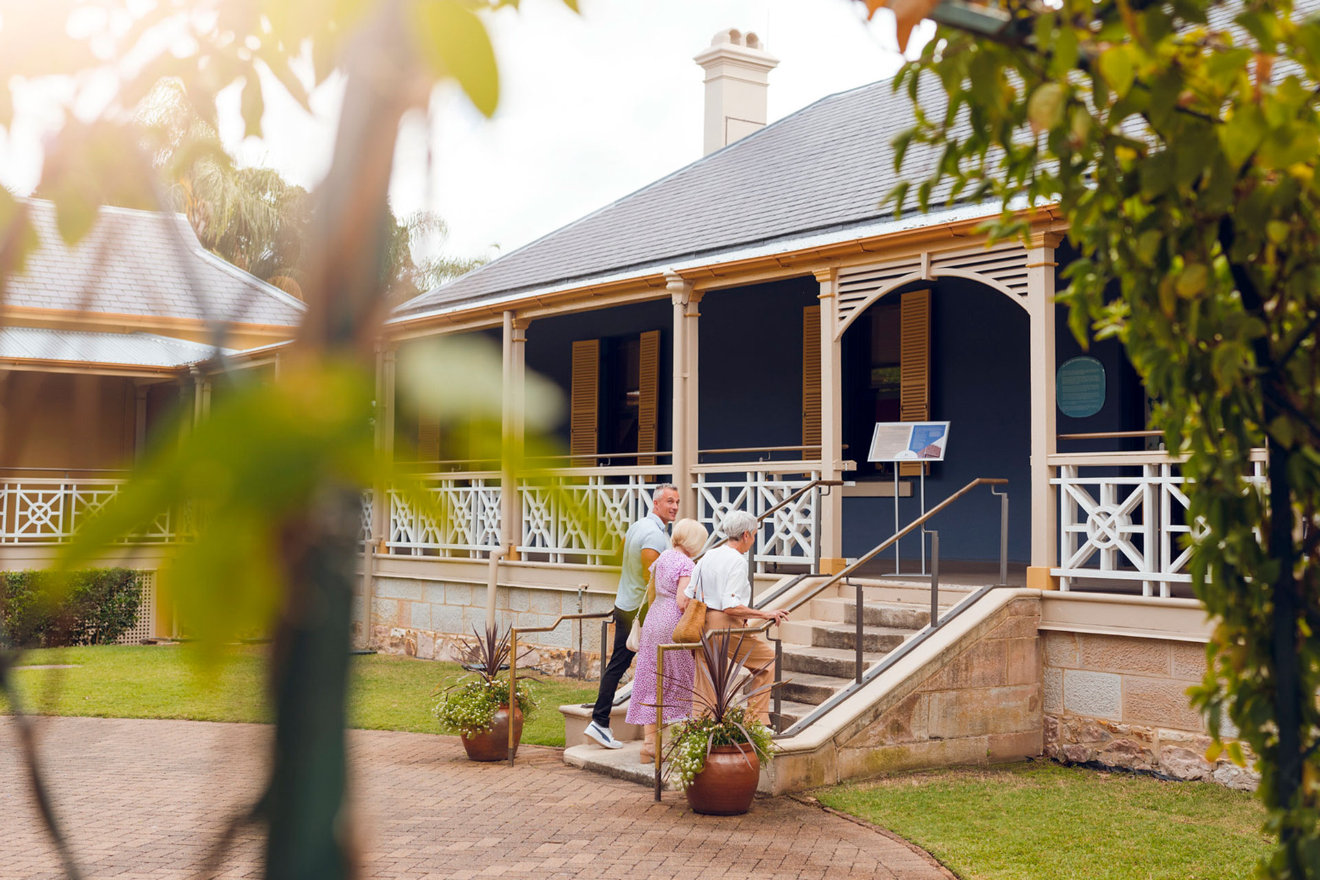 Three people walking up stairs to the entry of historic Newstead House with white fretwork ballustrade