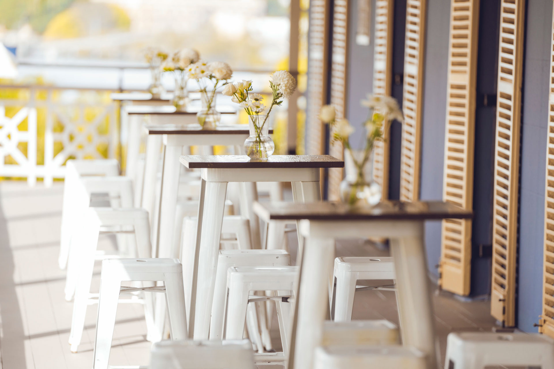 Verandah of Newstead House set with tall tables with vases of white flowers and white high seats