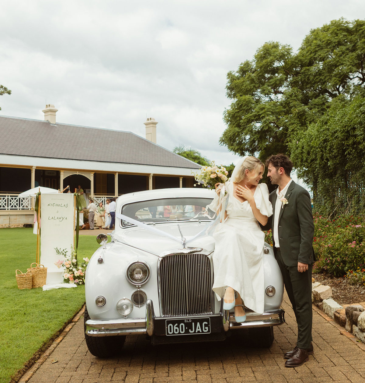 Bride seated on the bonnet of a vintage car looking into the eyes of her standing groom in front of Newstead House