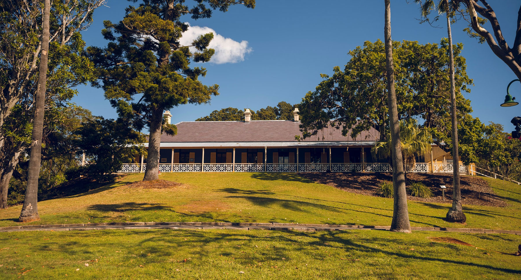 Exterior view of Newstead House from Newstead Park with a green lawn and large trees growing on each side of the house that is lengthways with a white patterned balustrade