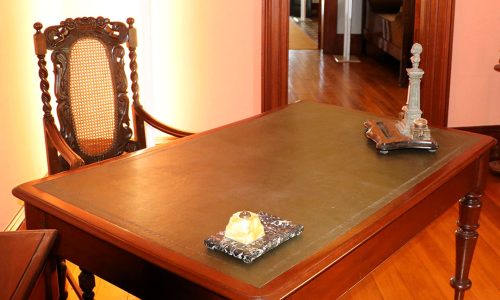 Wooden table with dark blue leather surface wooden chair behind table writing implements including glass ink well on table